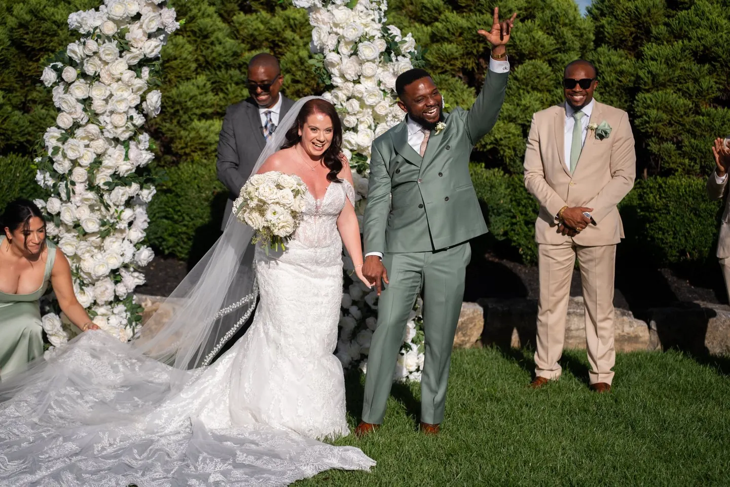 A newly married couple walks hand in hand beneath white floral arches